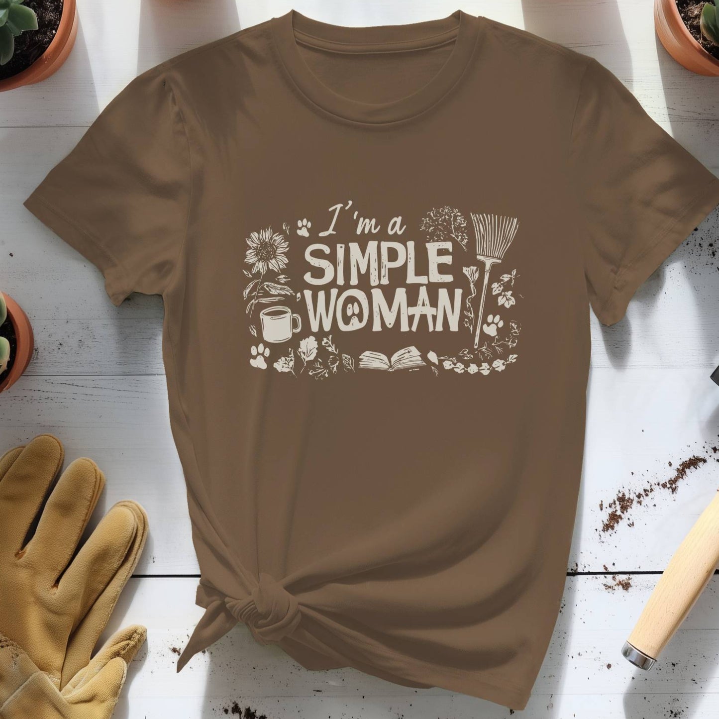 Brown t-shirt with 'I'm a Simple Woman' text on a wooden surface with gardening tools and plants.