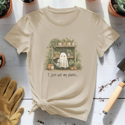 Beige t-shirt with a ghost and plants graphic and text, placed on a wooden surface with gardening tools and plants.